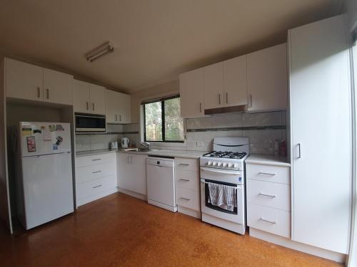 una cucina con armadietti bianchi, piano cottura e frigorifero di Sea'Renity Cottage a Venus Bay