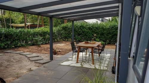 eine Terrasse mit Tisch und Stühlen unter einer Pergola in der Unterkunft Boshuisje met kachel "Huisje van Loof" op de Veluwe in Nunspeet