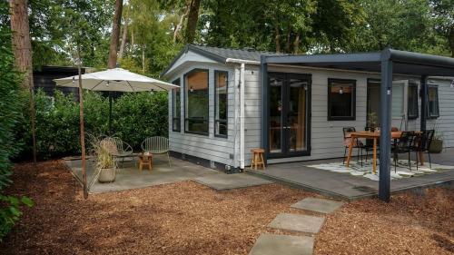 a small white cabin with a table and an umbrella at Boutique Boshuisje op de Veluwe in Nunspeet