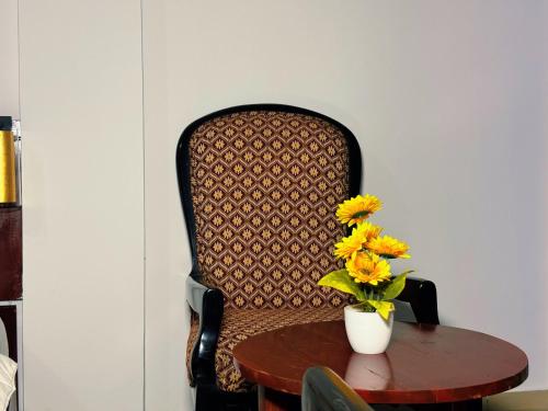 a chair with a table and a vase with yellow flowers at Hotel BKBG in Lomé