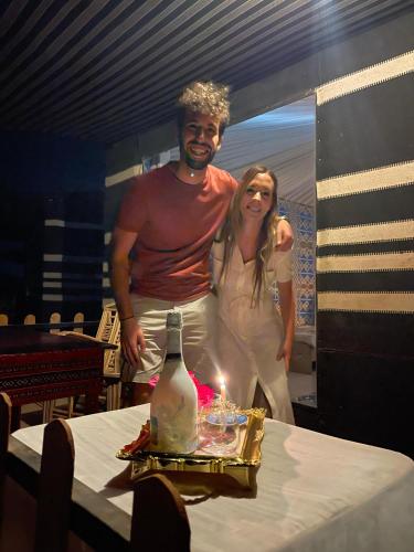 a man and a woman standing next to a table with a candle at Wadi Rum Magic Camp in Wadi Rum