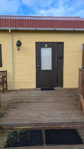 a yellow building with a black door and a wooden deck at Staðarhóll Guesthouse Room B in Þingeyjarsveit