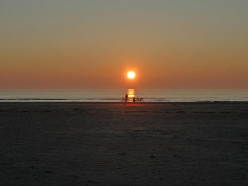 a sunset on the beach with a lighthouse in the ocean at Holiday Home Freek - 400m from the sea by Interhome in Lakolk