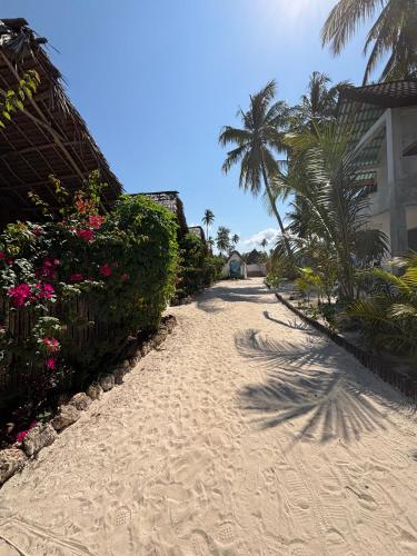 a dirt road with flowers and palm trees and a building at Beach Bohème in Paje