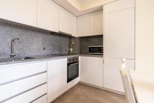a kitchen with white cabinets and a sink at Modern & Sleek Flat | Terrace & Garage by HostWise in Porto