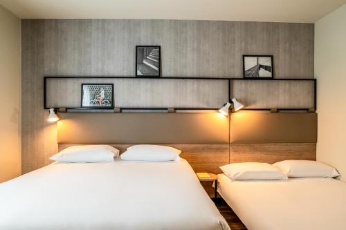 two beds in a room with two lamps on the wall at ibis Bordeaux Nord Carbon Blanc in Carbon-Blanc