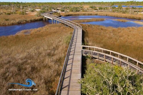a wooden boardwalk over a river with a bridge at Gateway To The Gulf in Pensacola