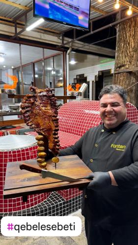 a man holding a cutting board with a piece of meat at Qafqaz Fountain Villa in Gabala