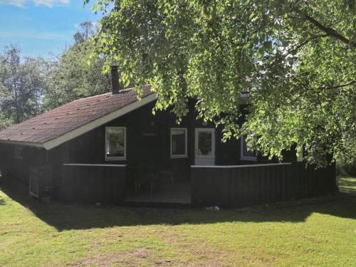ein kleines schwarzes Haus auf einem Feld mit einem Baum in der Unterkunft 6 person holiday home in Gedser-By Traum in Gedser