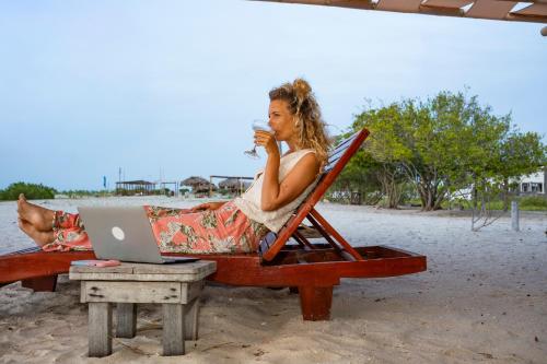 a woman sitting in a chair on the beach with a laptop at Watu Kite House in Mayapo