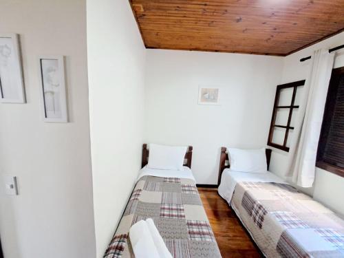 two beds in a room with white walls and wooden ceilings at Charme nas montanhas com lareira in Campos do Jordão