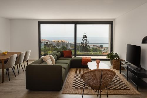 a living room with a green couch and a large window at Outsite Ericeira Praia do Sul - Work, Connect, Explore in Ericeira
