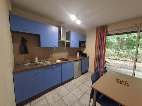 eine Küche mit blauen Schränken, einem Tisch und einem Fenster in der Unterkunft Cottage Le Vau 3 