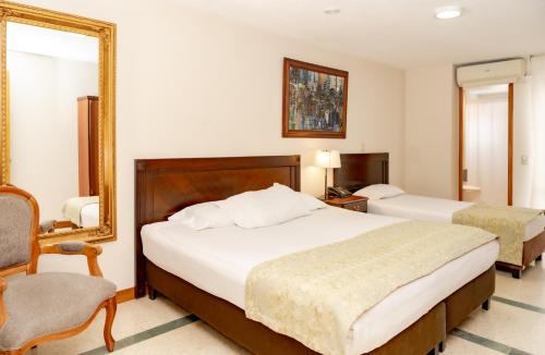 a bedroom with two beds and a mirror and a chair at Hotel San Pedro del Fuerte in Medellín