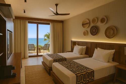 two beds in a hotel room with a view of the ocean at JAZ Elite Aurora in Michamvi