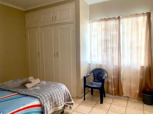 a bedroom with a bed and a chair and a window at Apartment at Jenner in Windhoek