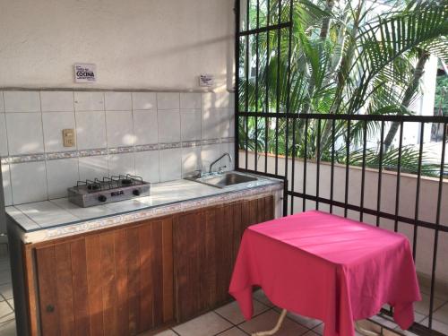 a kitchen with a sink and a table with a pink stool at Hotel Villa Tulipanes in Zihuatanejo