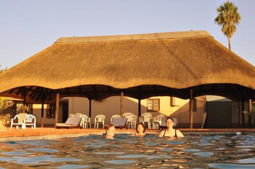 un gruppo di persone che nuotano in una piscina con tetto di paglia di Kashana Namibia a Omaruru