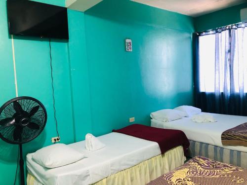 two beds in a room with blue walls and a fan at Chaleanor Hotel in Dangriga