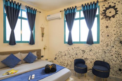 a bedroom with a bed with blue curtains and two chairs at Shalom Backpackers Anjuna Goa in Anjuna
