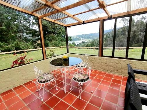 eine Terrasse mit Tisch und Stühlen in einem Raum mit Fenstern in der Unterkunft El Rincón del Lago Escapada Privada en el Sisga in Chocontá