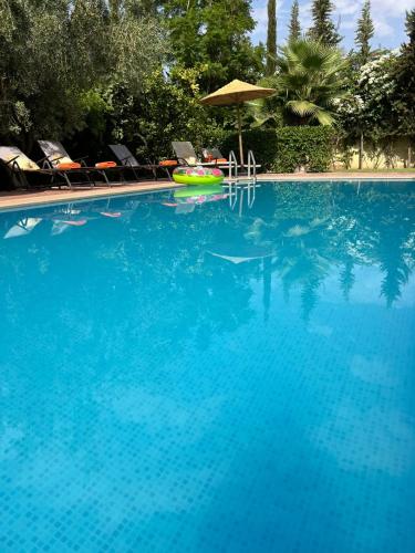 a large blue swimming pool with chairs and an umbrella at Chambre d'hôtes dans luxueuse villa avec piscine in Had Abdallah Rhiat