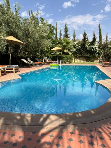 a large blue swimming pool with chairs and umbrellas at Chambre d'hôtes dans luxueuse villa avec piscine in Had Abdallah Rhiat