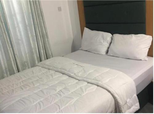 Cama con sábanas blancas y almohadas junto a una ventana en Epe Hotels & Suites, en Epe