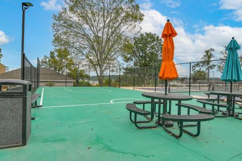 a tennis court with two tables and an orange umbrella at Table Rock Lake Retreat Steps to Water and Pools! in Kimberling City