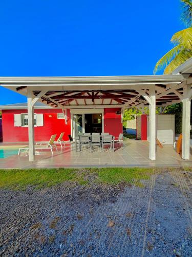 a patio with chairs and tables and a red building at Villa SAADA cosy avec piscine, jacuzzi et sauna in Le Vauclin