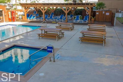 a pool with wooden tables and benches next to a swimming pool at Beach Access Condo with Pool, Hot Tub Area & BBQ - Gulfview I - unit 213 in South Padre Island
