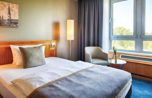 a hotel room with a bed and a chair and a window at Leonardo Hotel Köln Bonn Airport in Cologne