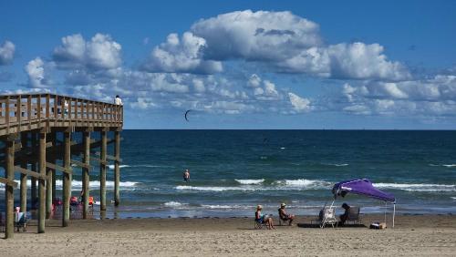 people on a beach with a pier and the ocean at Los Cabos I #5 condo in South Padre Island