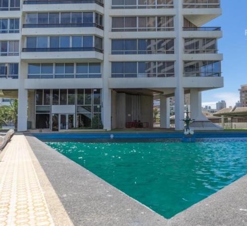 a building with a swimming pool in front of a building at Habitación frente a Muelle Vergara en un departamento in Viña del Mar
