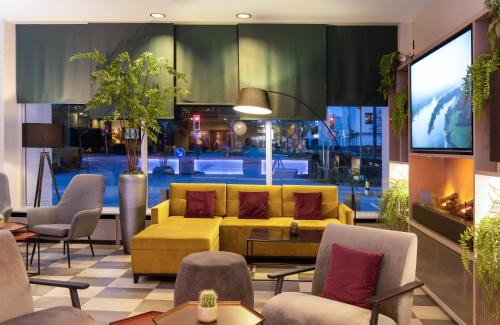d'un salon avec un canapé et des fauteuils jaunes. dans l'établissement Leonardo Hotel Düsseldorf Airport Ratingen, à Ratingen