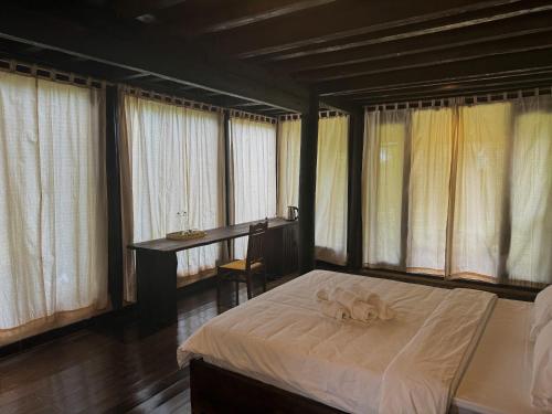 a bedroom with a bed with a desk and windows at Cọ Retreat Da Bac in Hòa Bình