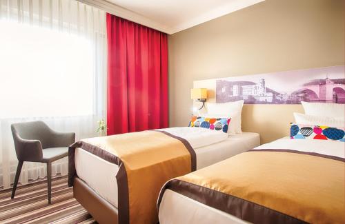 a hotel room with two beds and a chair at Leonardo Hotel Heidelberg in Heidelberg
