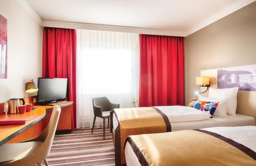 a hotel room with two beds and a desk and a television at Leonardo Hotel Heidelberg in Heidelberg