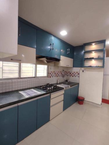 Una cocina con gabinetes azules y un refrigerador blanco. en Vrindavan place, en Chhatikara