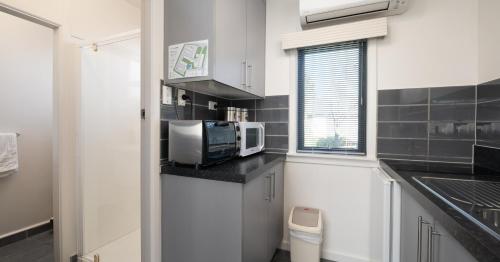 a small kitchen with a microwave and a sink at Grove Park Motor Lodge in Blenheim