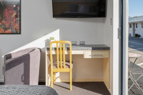a room with a desk with a tv and a chair at Grove Park Motor Lodge in Blenheim
