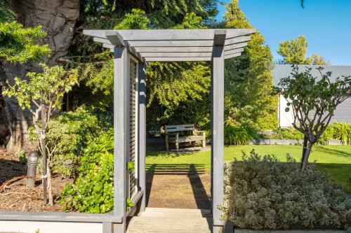 a wooden archway in a garden with a bench in the background at Grove Park Motor Lodge in Blenheim