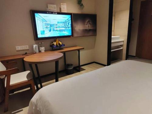 a room with a bed and a table and a television at JTOUR Inn Wuhan Textile University in Wuhan