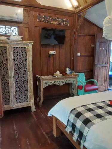 a bedroom with a bed and a table and a tv at Buratwangi Joglo House in Kerobokan