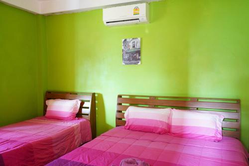 a green room with two beds with pink sheets at Ban Rai Rabeang Mok in Khao Kho