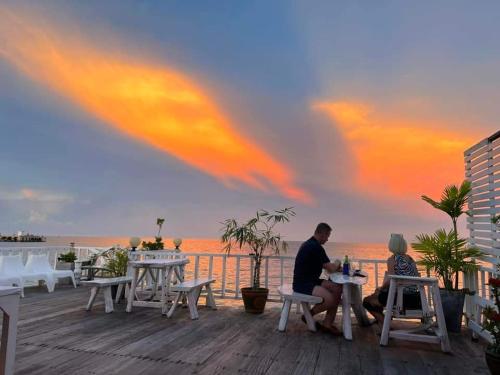 a man and woman sitting at tables on a deck with the ocean at Karoon Sea View Lodge in Hua Hin
