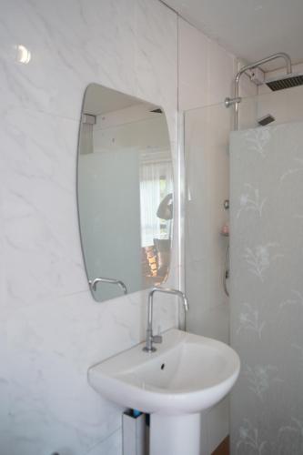 a white bathroom with a sink and a mirror at Ban Rai Rabeang Mok in Khao Kho