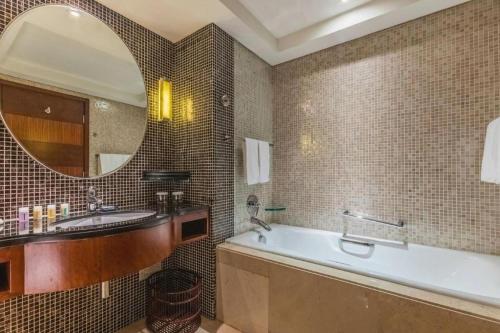 a bathroom with a tub and a sink and a mirror at Kunshan Newport Hotel in Suzhou