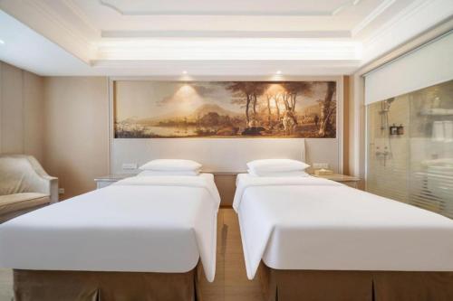 two beds in a room with a painting on the wall at Vienna Hotel Guiyang Jiaxiulou Jichang Road in Guiyang