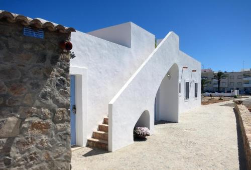 a white building with a staircase next to a stone wall at Moinhos das Marés in Fuzeta
